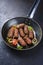 Traditional Croatian cevapi spicy meat ball rolls with tomatoes and onion rings in a skillet