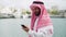 Traditional dressed arab businessman with smartphone in port, reading internet news on mobile phone