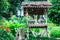 Traditional drinking water earthenware container under wooden shade shelter in green tropical ornamental garden in natural park ba