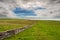 Traditional dry stone fence in a field with green grass. West coast of Ireland. Nobody. Beautiful cloudy sky. Rural area