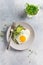 Traditional English breakfast with fried eggs with arugula microgreen in gray ceramic plate on gray concrete old background. Top