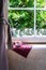 Traditional English tea in a cup over a scottish tartan wipe placed on a white-framed window ledge overlooking some trees