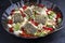 Traditional fried Greek cod fish filet casserole with feta cheese and vegetable in a rustic wrought iron pan