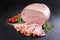 Traditional German boiled ham as piece and sliced decorated with tomatoes and herbs on black rustic board