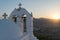 Traditional Greek beauty with a church against the sun on top of a mountain.