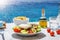 A traditional Greek farmers salad with fries and olive oil in front of the mediterranean sea