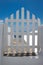 Traditional Greek island architecture, a white gate leading to a pathway with the sea in the background.