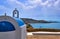 Traditional Greek Orthodox church with blue dome and bell tower in typical Greek coastal or island landscape at summer