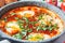 Traditional Israeli shakshuka in gray frying pan. Fried eggs in tomato sauce, close-up