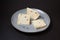 Traditional Italian Caciotta cheese with black pepper on grey plate, close-up. Dark background, selective focus