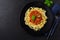 Traditional Italian dish fettuccine pasta with bolognese sauce, basil and parmesan cheese in black plate on dark wooden background