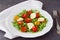 Traditional Italian salad with cherry tomato, ruccola, mozzarella, olive oil wine vinegar on a white plate on a grey