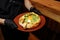 Traditional khachapuri with spinach leaves in the hands of a waiter in black gloves