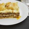 Traditional lasagne served on a white round plate over dark surface, side view. Close-up