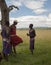 Traditional Masai men, talking in green field, one leaning against tree