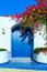 Traditional Mediterranean house with a stone fence and a large blue door decorated with flowering plants. Front view