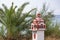 Traditional and memorial roadside small chapel or church in Greece with palm tree and sea in background