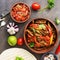 Traditional mexican dish fajitas meat with vegetables and salsa sauce on a dark rustic background. Flat lay, overhead