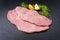 Traditional raw veal schnitzel from topside with herbs and lemon slice on black background