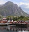 Traditional red colorful Norwegian fishing houses in Reine with mountains on the background, Lofoten Islands