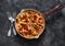 Traditional Roman pasta - bucatini amatricana in a pan on a dark background, top view