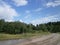 A traditional Russian landscape with a dirty, broken road that goes into the distance, with a forest and a river in the background