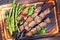 Traditional Russian shashlik on a barbecue skewer with green asparagus and paprika on a burnt wooden cutting board