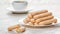 Traditional savoiardi biscuits or ladyfingers cookies on a plate and white cup of coffee on background