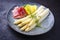 Traditional steamed white asparagus with cured ham and boiled potatoes garnished with butter sauce on a Nordic design plate