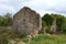 Traditional stone house ruins with missing roof partially overgrown with crawler plant surrounded with dense vegetation