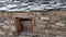 Traditional stone hut in Uttarakhand, India, featuring a wooden window set within a rugged stone wall, showcasing local