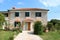 Traditional stone Mediterranean villa with new window blinds and front wooden doors surrounded with grass and stone tiles path