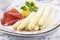 Traditional style steamed white asparagus with gammon and boild potatoes with sauce hollandaise on a classic design plate