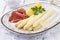 Traditional style steamed white asparagus with gammon and boild potatoes served with sauce hollandaise on a classic design plate