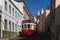 Traditional tram in a narrow street in the Alfama neighbourhood with the Sao Vincente de Fora Church on the background