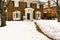 Traditional two story brick house with bay windows and pillared porch in the snow with the sidewalk cleared