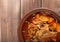 Traditional Ukrainian borsch with meat on the edge, in a brown clay bowl, on a wooden background.