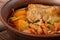 Traditional Ukrainian borsch with meat on the edge, in a brown clay bowl, on a wooden background.