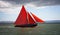 Traditional wooden boat with red sail.