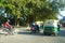 Traffic of Cars, Autos and Bikes on Indian Road in day time. People are present standing under trees away from sun light. : Punjab