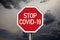 Traffic sign with dark cloudy sky with message Stop Covid 19