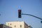 A traffic signal with 4 lights with the red light on surrounded by white buildings and clear blue sky in Pasadena California