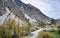 The trail at the foot of the picturesque rocky mountain slope goes up between the bright autumn trees.