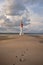 A trail of footprints leads to a lighthouse in the distance, a symbol of hope and destination