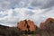 A trail at the Garden of the Gods leading to huge red rock formations rising up above pine trees on a cloudy day in Colorado