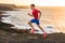 Trail runner sport fitness man ultra running on ocean cliff in sunset. Sports athlete jogging training outdoors in rocky landscape