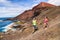 Trail running couple runners racing on mountain path in volcanic rocks nature landscape in summer outdoor. Ultra running