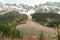 A trail surrounded by pine forest leading up into rugged, snowy mountains