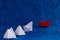 Trail of white paper boats following a red boat sailing on sea tide with copy space