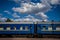 Train with blue wagons is standing on the platform against the background of a beautiful summer sky